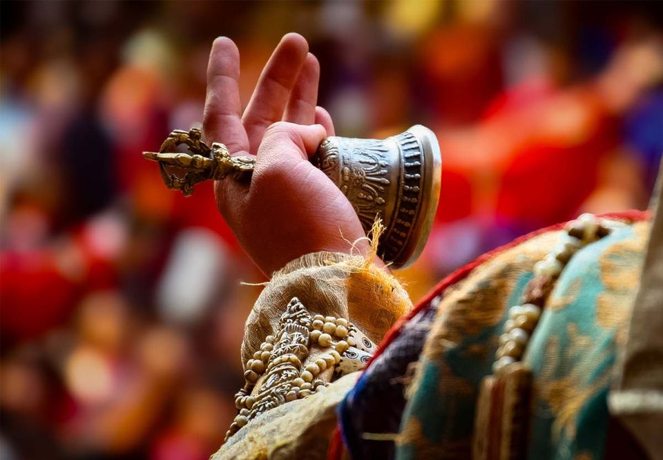 A hand raising a ritual bell and dorje above a festival crowd