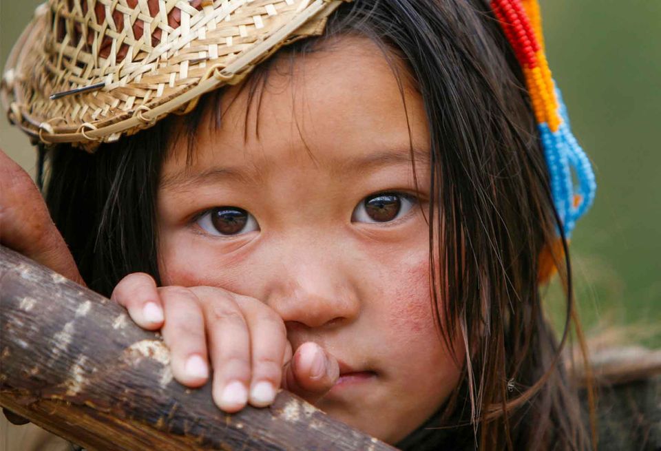 A young girl in a woven bamboo hat resting on a wooden rail