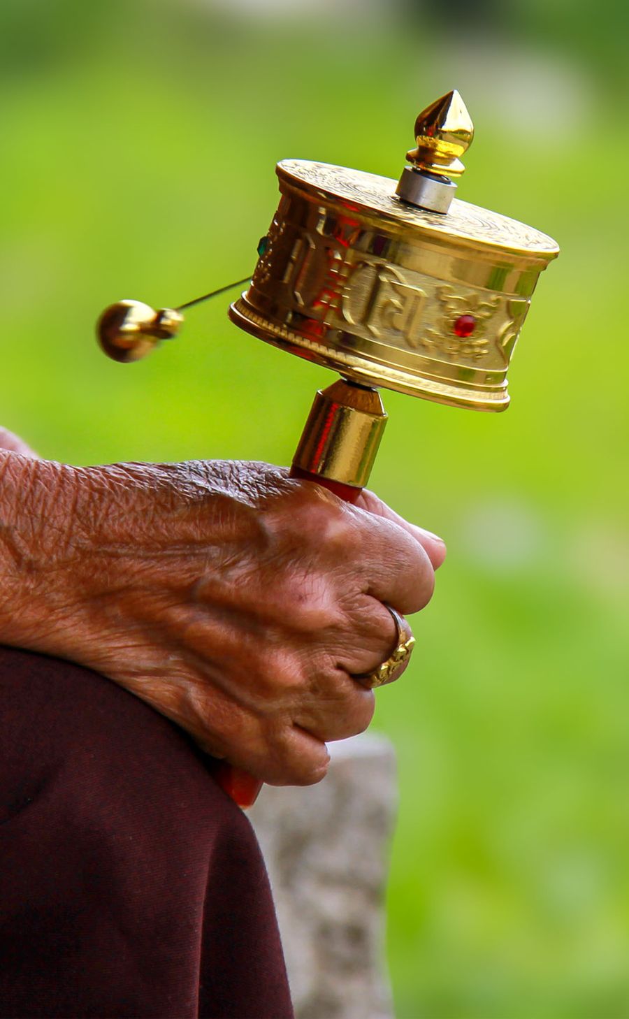 Weathered hands turning a brass handheld prayer wheel