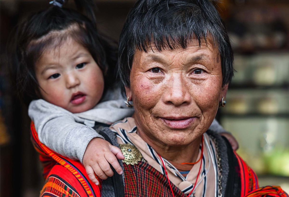 A smiling Bhutanese woman holding a small child on her back