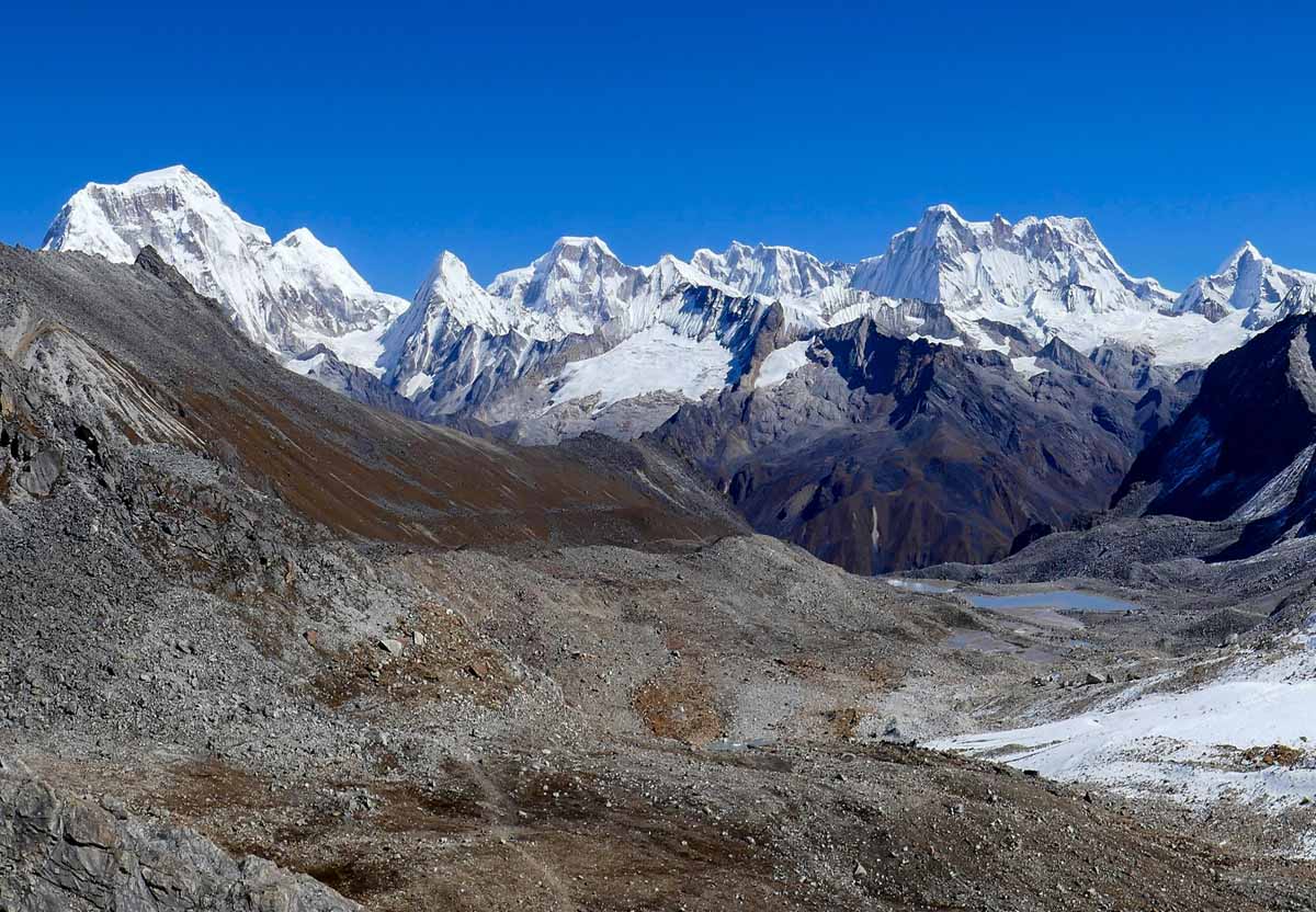 Trekkers crossing an alpine pass beneath snow-capped peaks