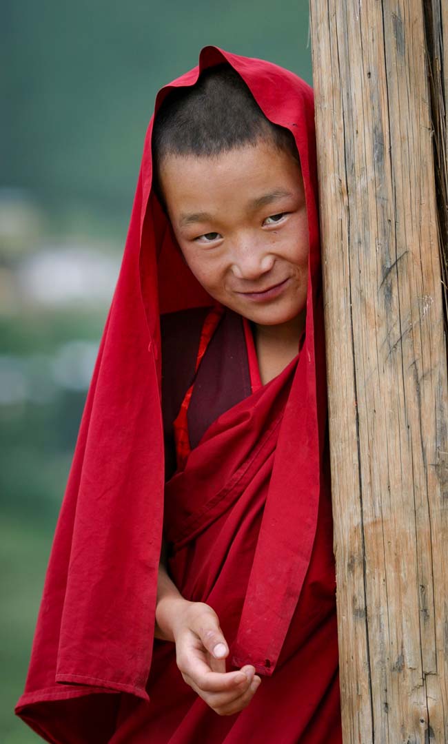 A young monk in red robes beside a monastery doorway