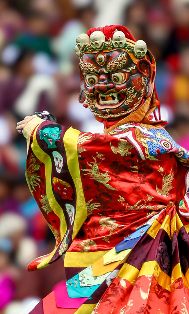 A masked dancer in brocade costume performing at a Bhutanese tsechu