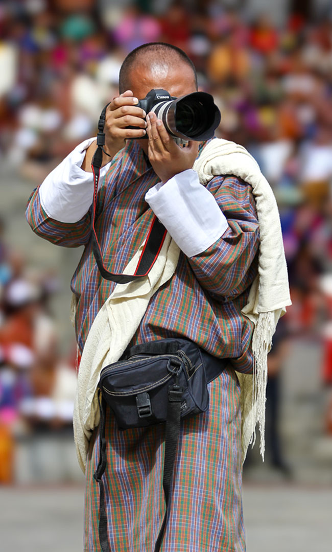 A Bhutanese photographer in a gho shooting a festival crowd