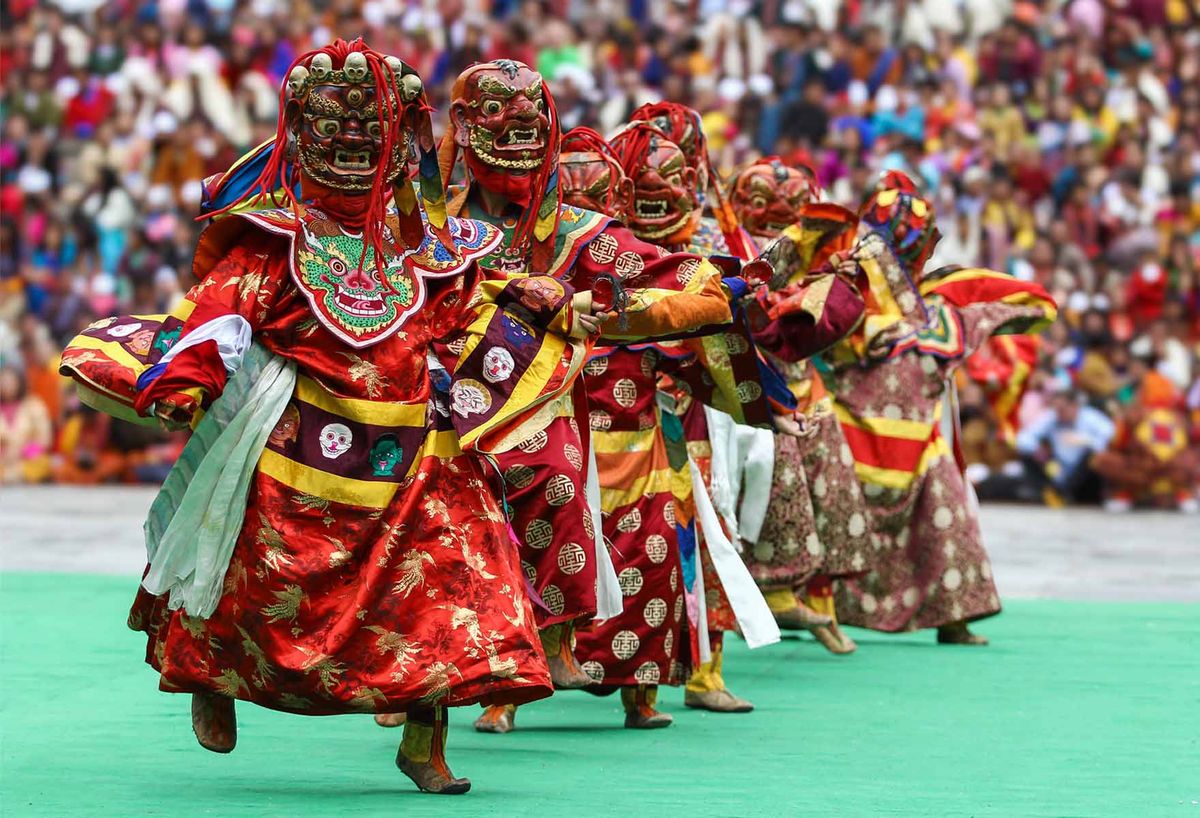 A line of masked dancers in red brocade robes mid-performance