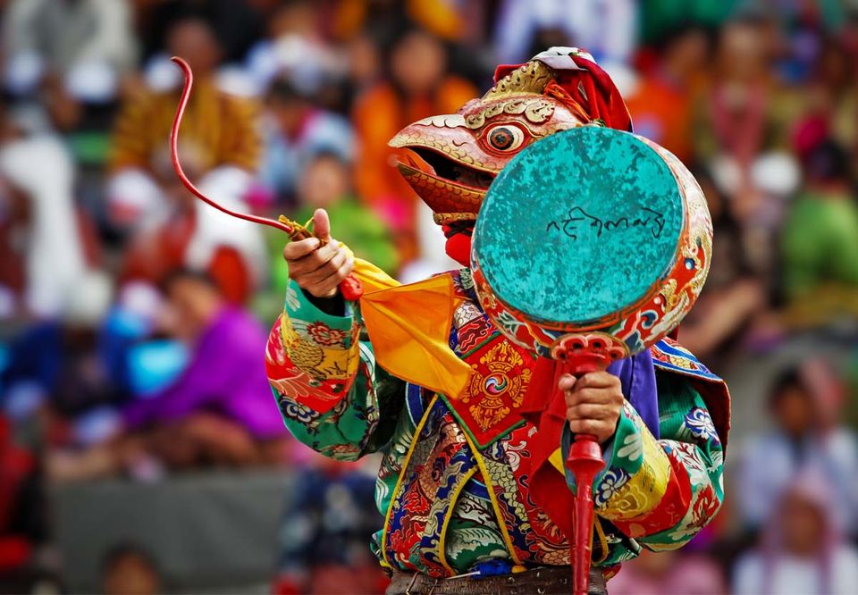 Masked dancer holding a turquoise ceremonial drum before a crowd