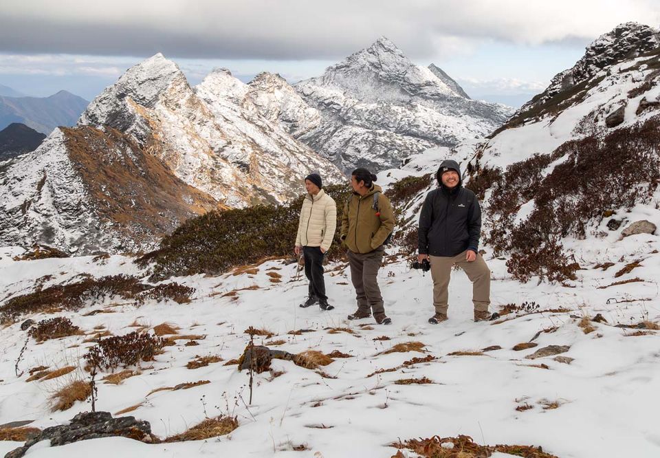 Walkers crossing a snow-dusted alpine slope beneath bare peaks