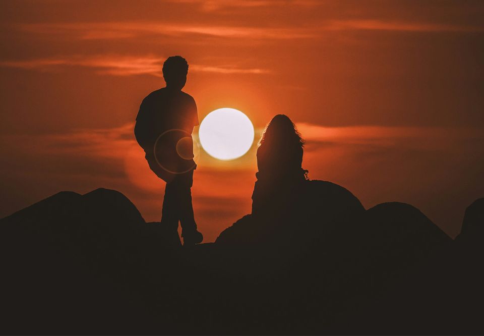 A couple silhouetted on a ridge as the sun sets behind them