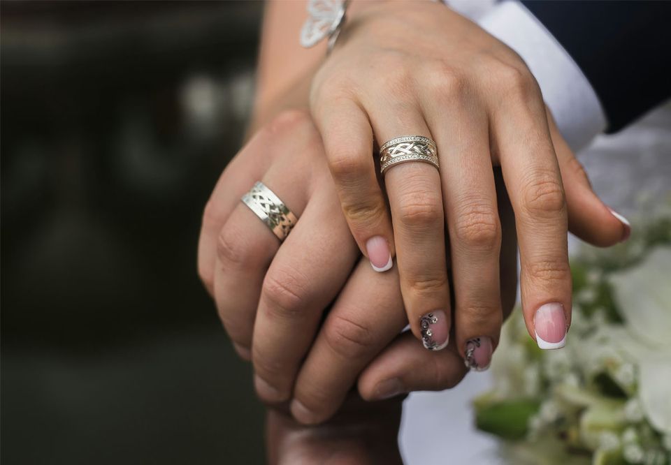 Two hands clasped together, both wearing wedding rings