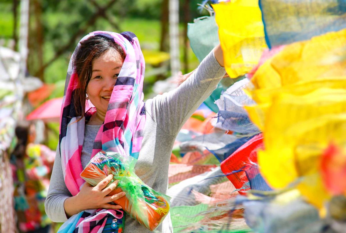 A woman tying colourful prayer flags on a hilltop