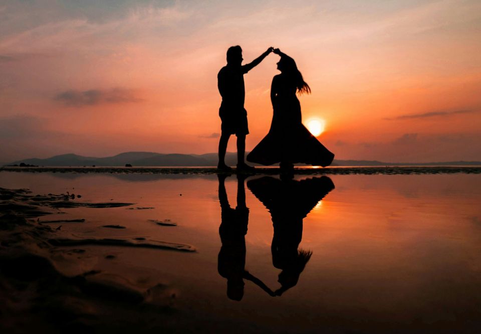 A couple dancing in silhouette, reflected in still water at sunset