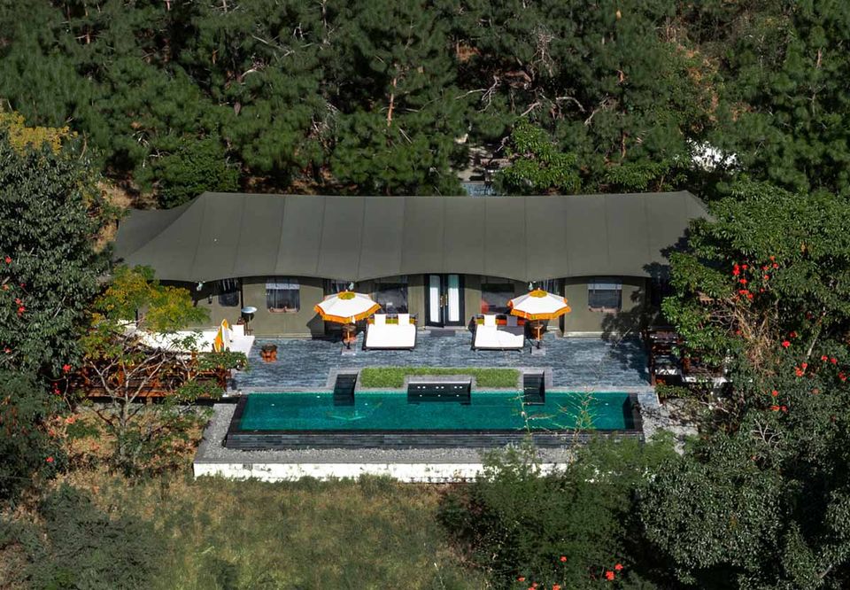 Aerial view of a luxury tented lodge and pool set in forest