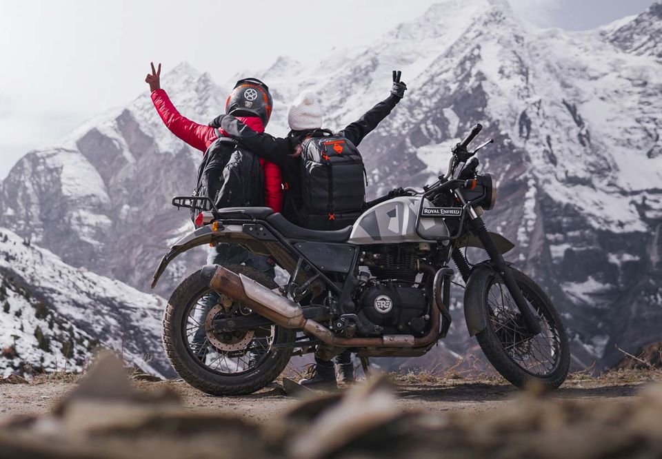 A rider celebrating beside a motorcycle below snow-capped peaks