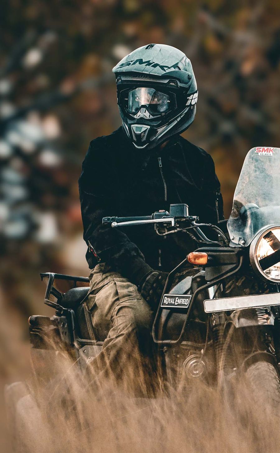 A helmeted rider on a Royal Enfield kicking up dust on a trail