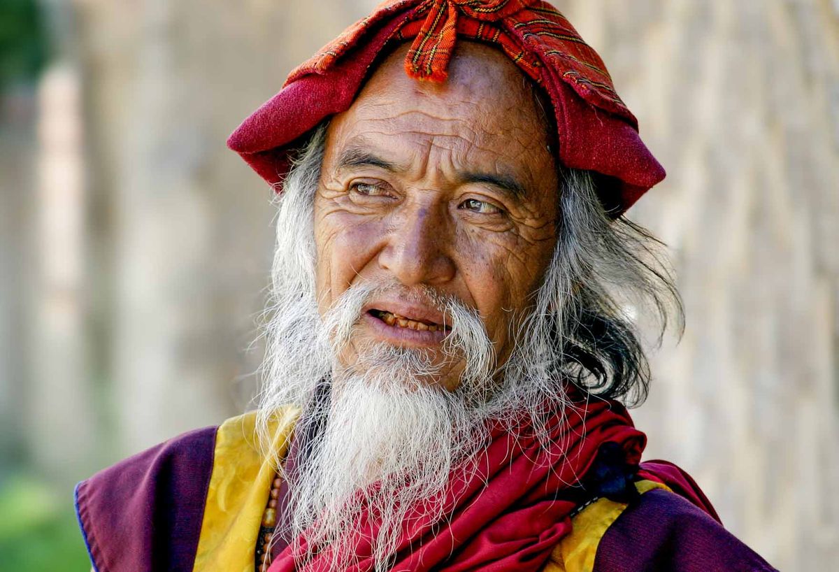 An elder in a red headdress and maroon robe smiling to camera