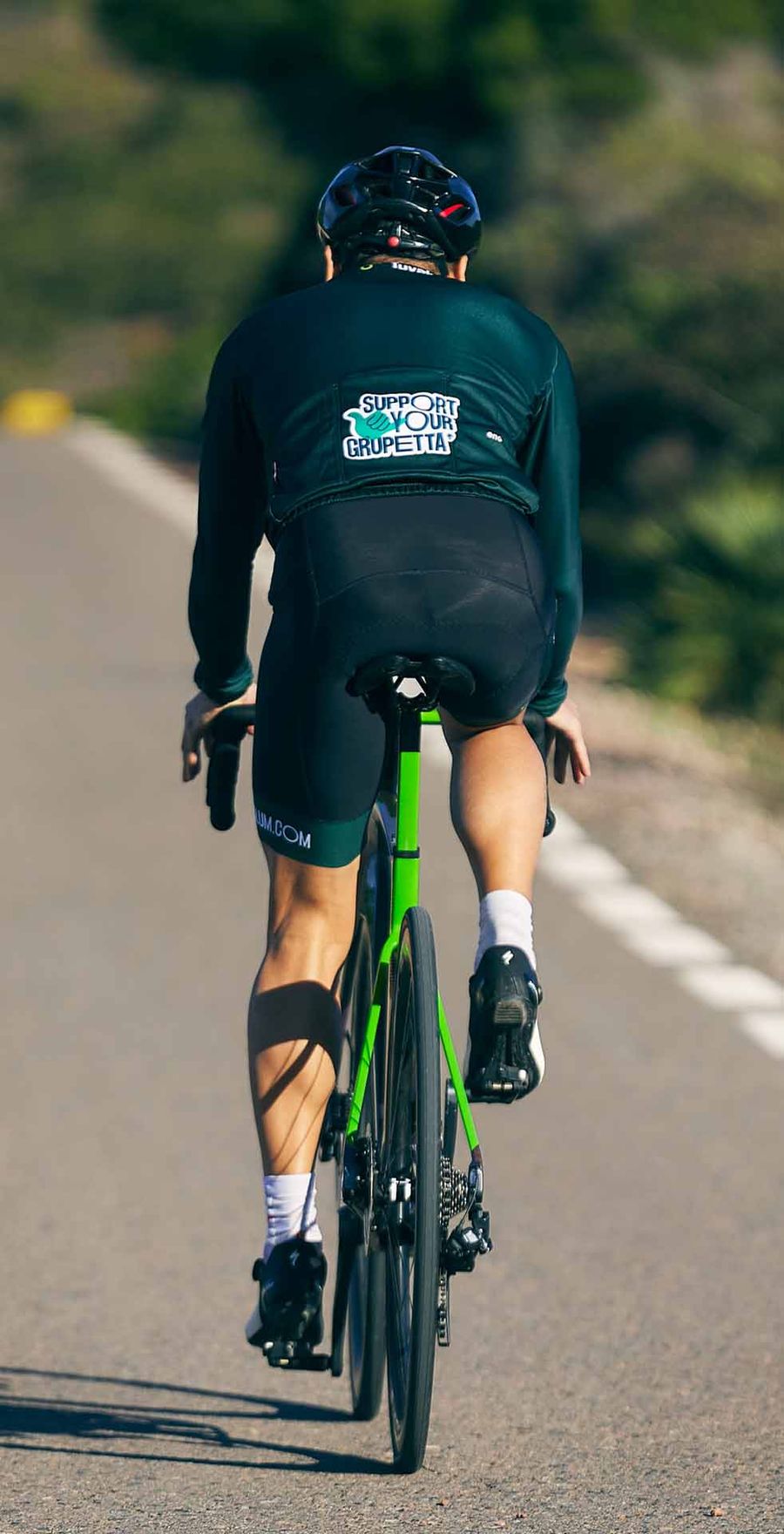 A cyclist seen from behind climbing a quiet paved road