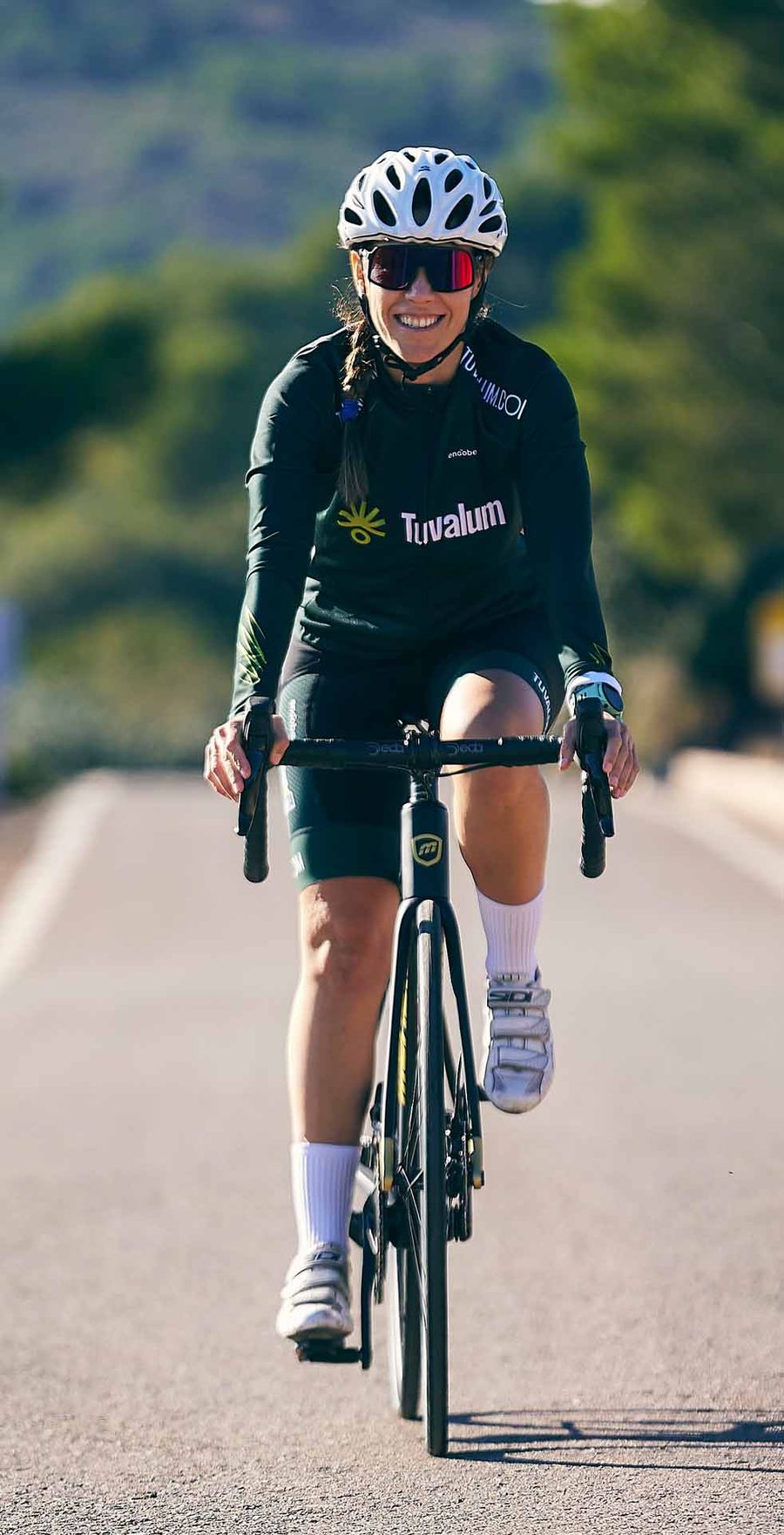 A smiling cyclist riding toward the camera on a mountain road