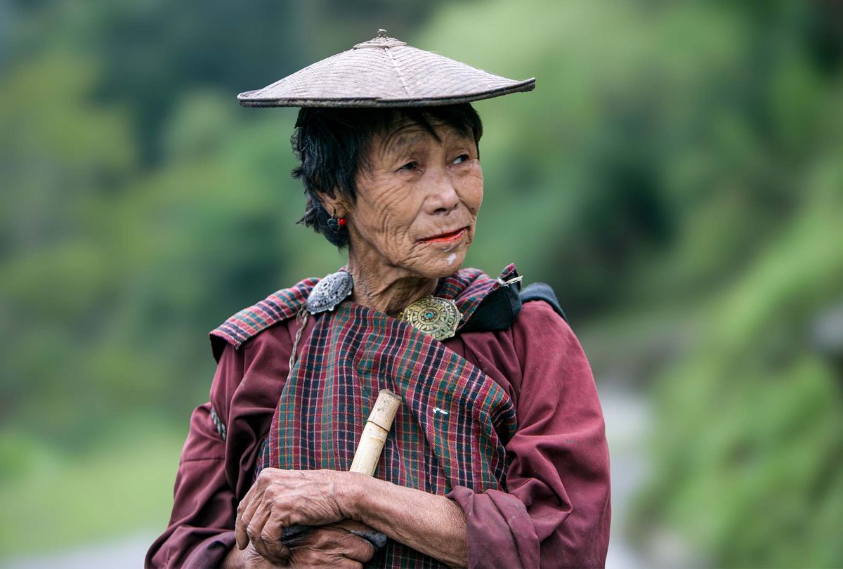 An elderly woman in a woven bamboo hat and traditional dress