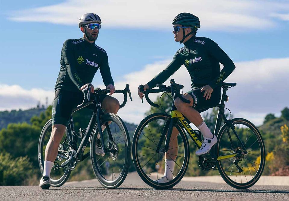 Two cyclists pausing side by side on a sunlit hillside road