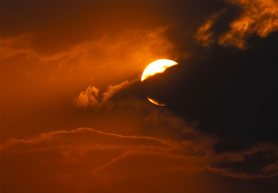 The sun breaking through burning orange clouds over Bhutan's hills