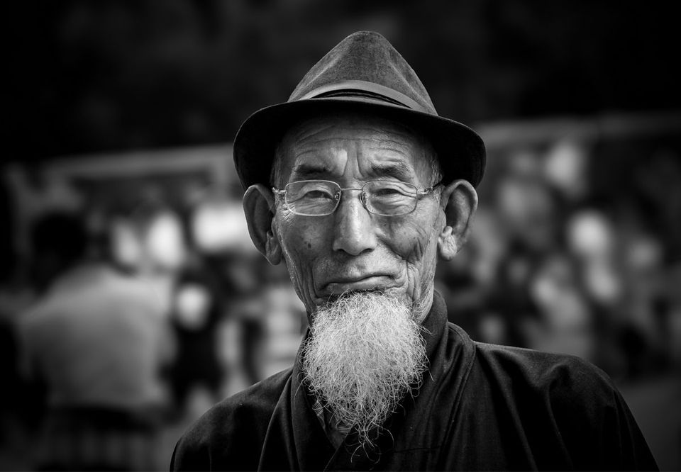 Black and white portrait of a bearded Bhutanese elder in a felt hat