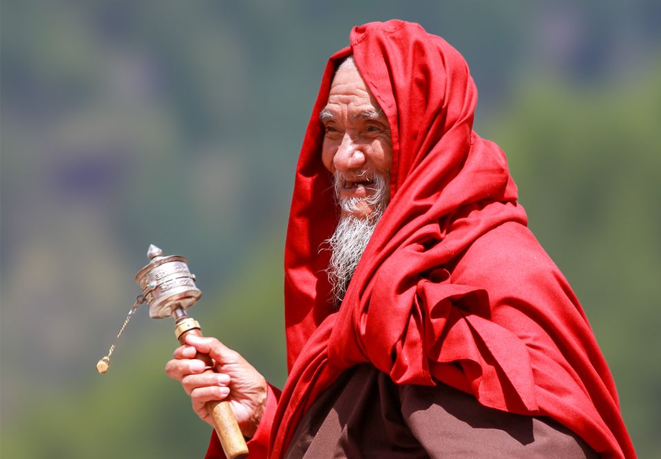 A Bhutanese elder in red robes spinning a handheld prayer wheel