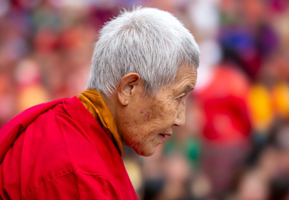 Elderly Bhutanese woman in crimson robes at a crowded festival