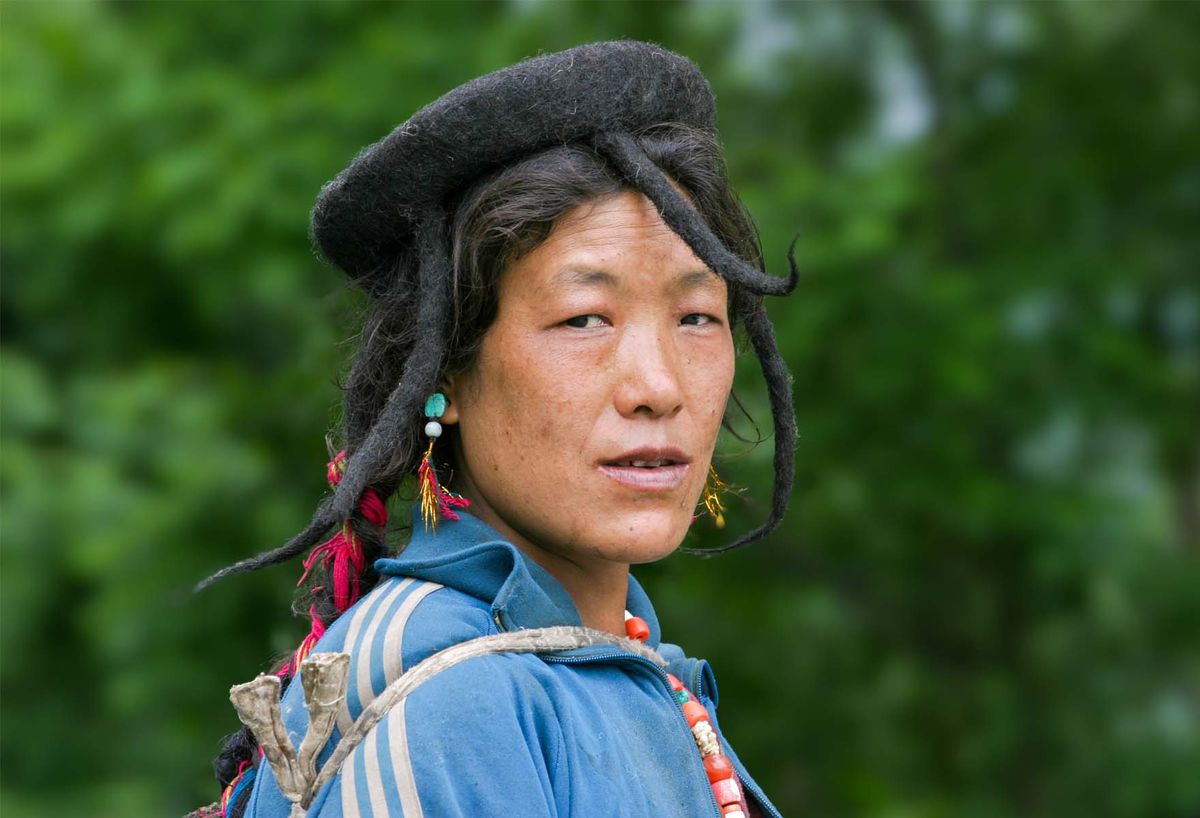 A Layap woman in a yak-hair hat and turquoise earrings against green forest