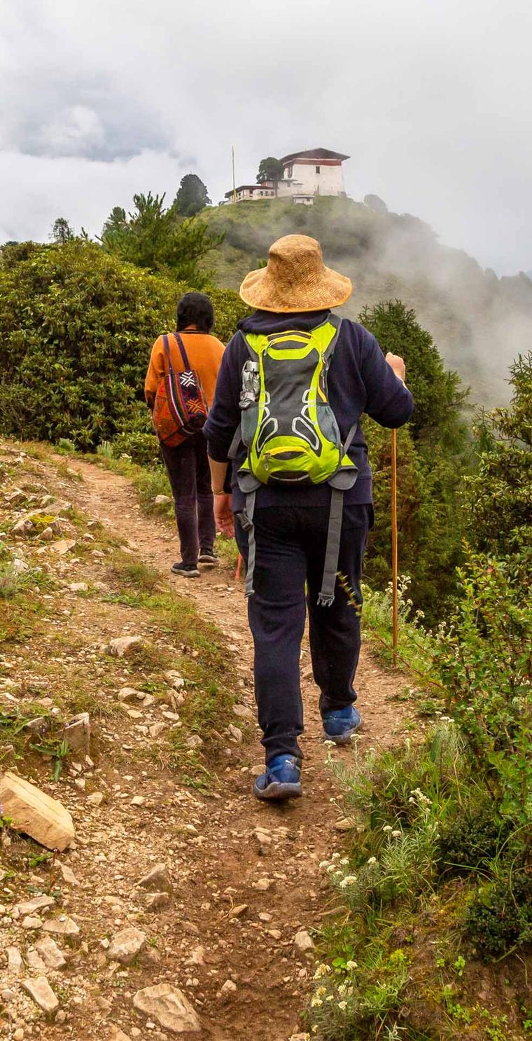 Two trekkers on a misty ridge trail below a hilltop monastery