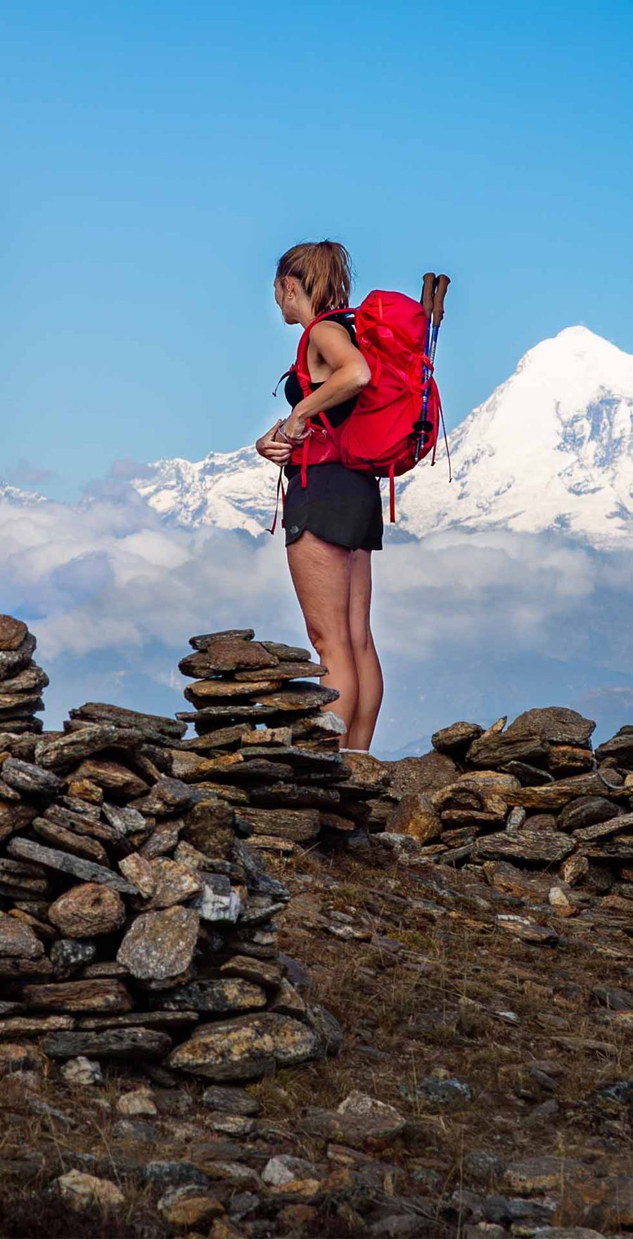 A trekker beside a stone cairn facing a snow-capped peak