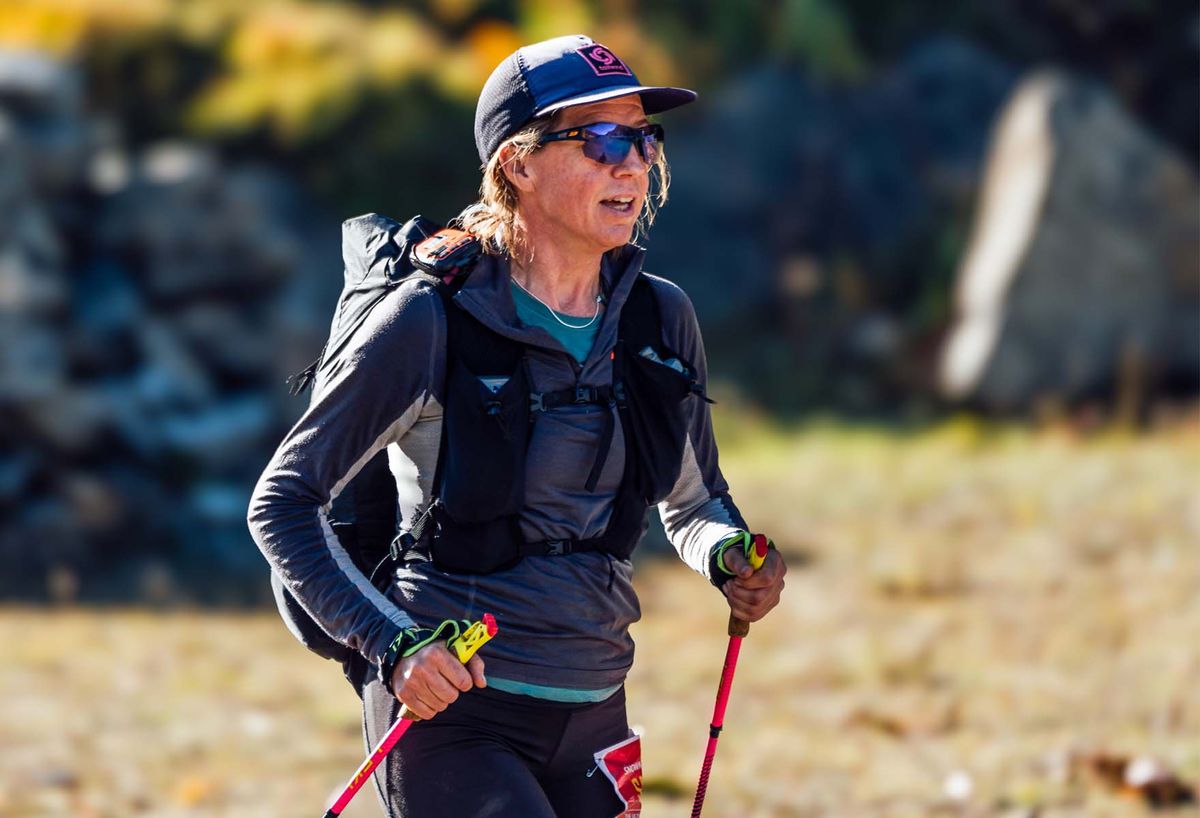 A trekker in a cap and sunglasses pausing with trekking poles