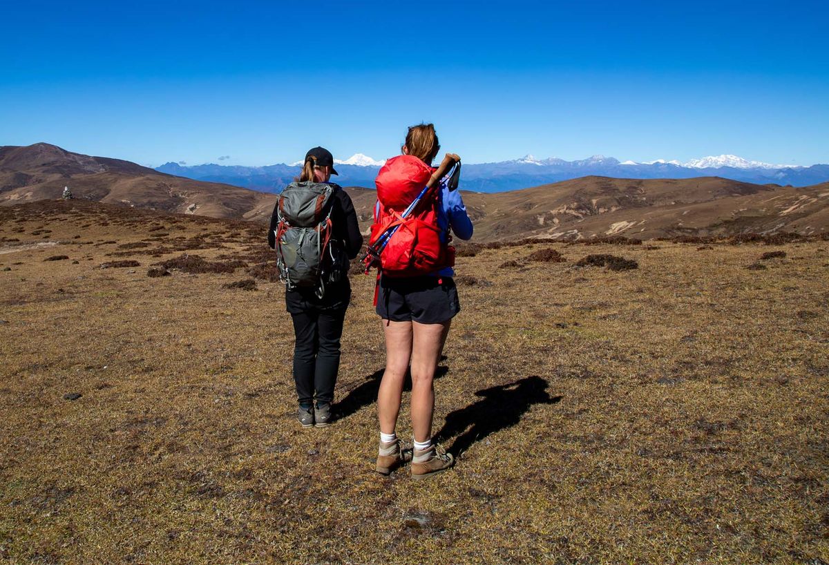 Two trekkers crossing open highland pasture toward distant peaks