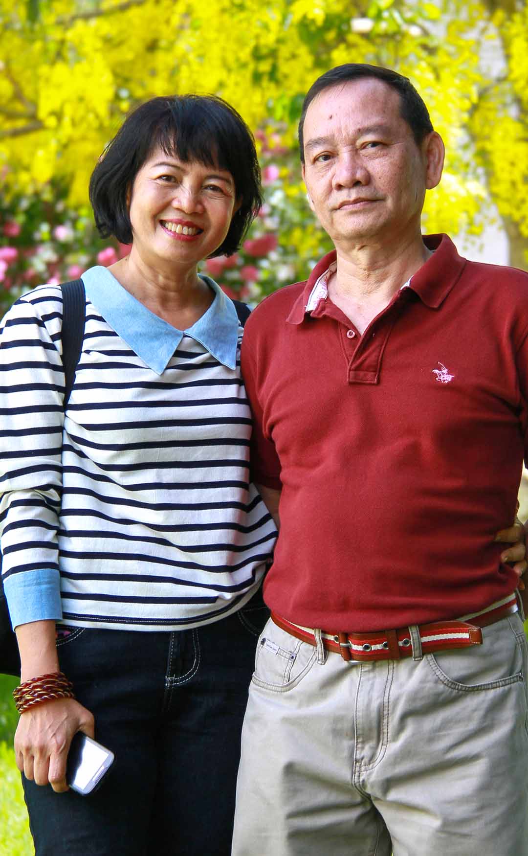 Kim and Jesung standing arm in arm beneath a flowering golden shower tree