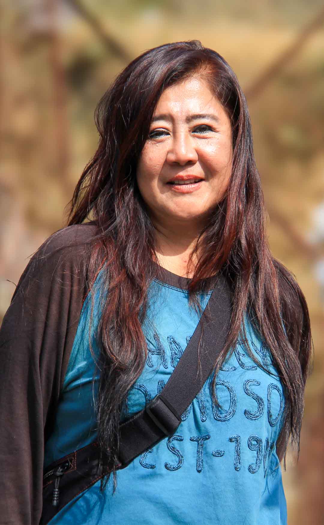 Vachira smiling outdoors in Bhutan on a sunny day, a camera bag strap across her shoulder
